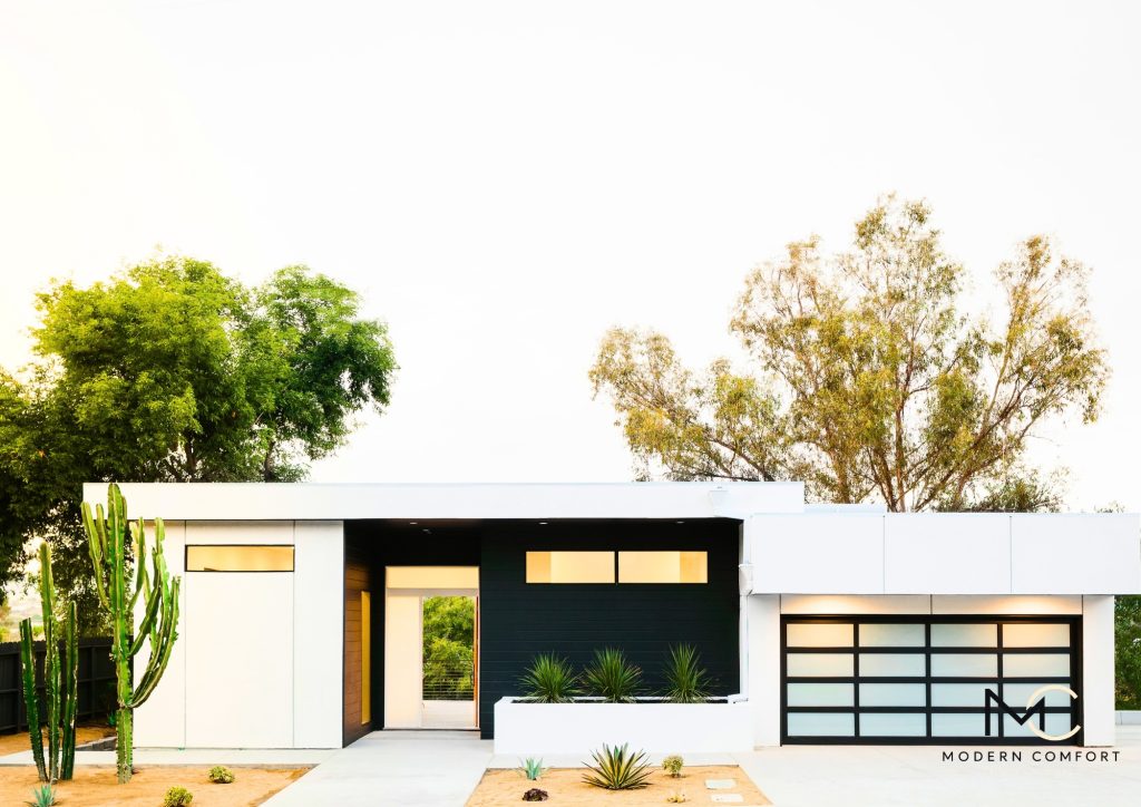 Single-story modern white home with glass garage door and desert landscaping