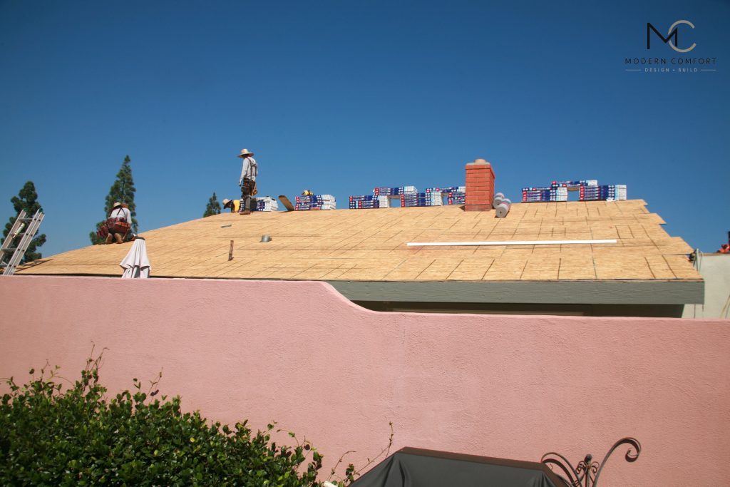Roofers installing new plywood roof sheathing on a stucco home