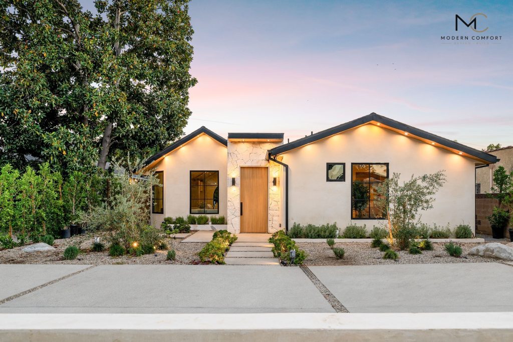 Single-story modern farmhouse-style home with warm exterior lighting at dusk